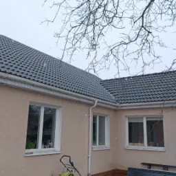 Dom z nowym, grafitowym dachem z dachówki ceramicznej, białe rynny, padający śnieg.