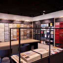 Wnętrze sklepu z ekspozycją próbek wykładzin w rożnych kolorach i fakturach, obok stołu z krzesłami i katalogów.