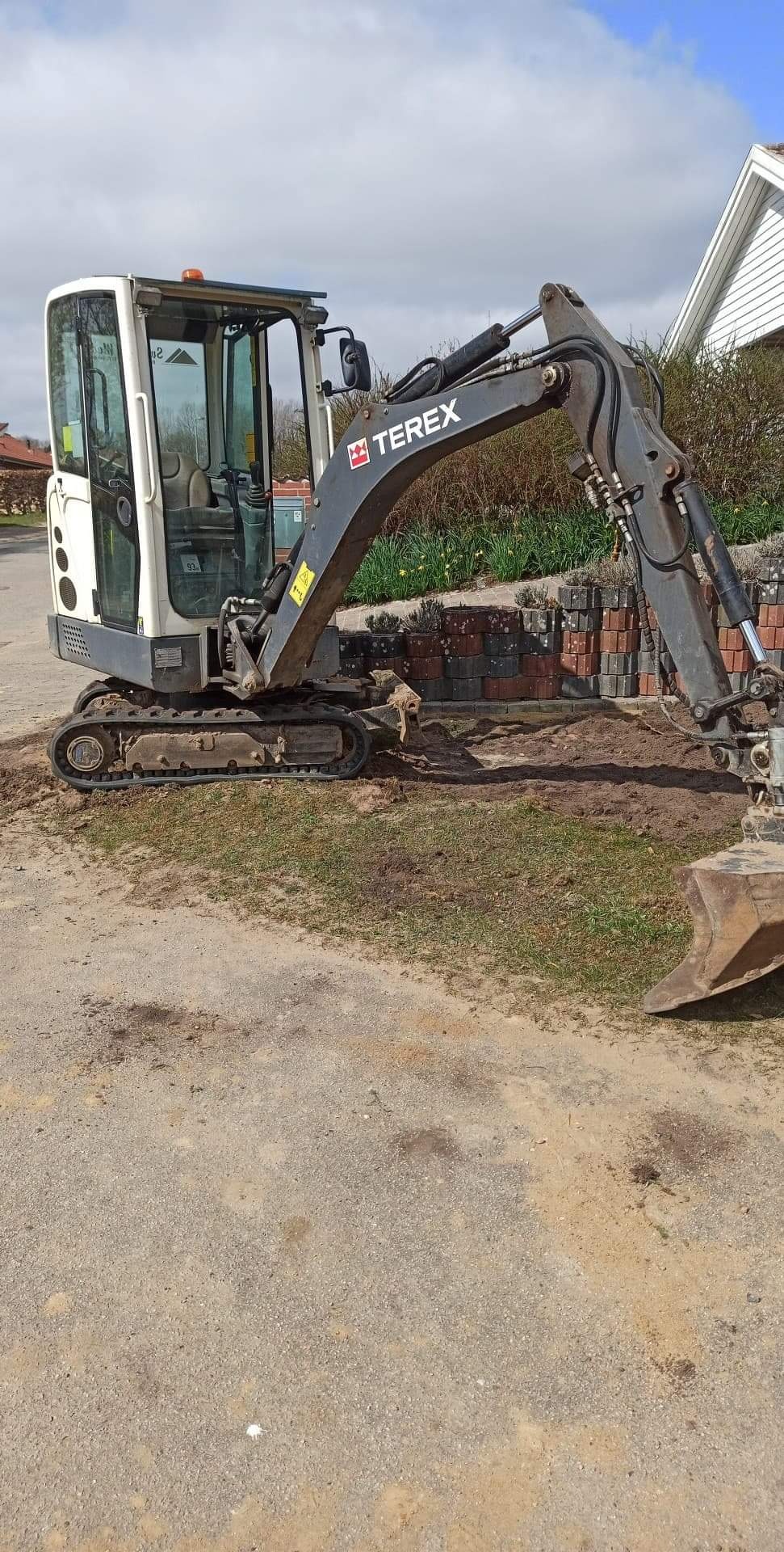 Mała koparka Terex na placu budowy, obok ułożone kostki brukowe, widok z boku.