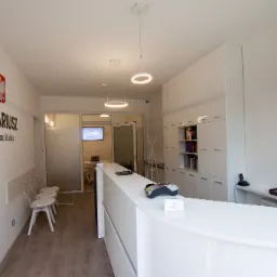 Jasne wnętrze kancelarii notarialnej z recepcją, logo z godłem Polski i nazwiskiem notariusza na ścianie, oraz widocznymi krzesłami dla klientów i oświetleniem w postaci okręgów.