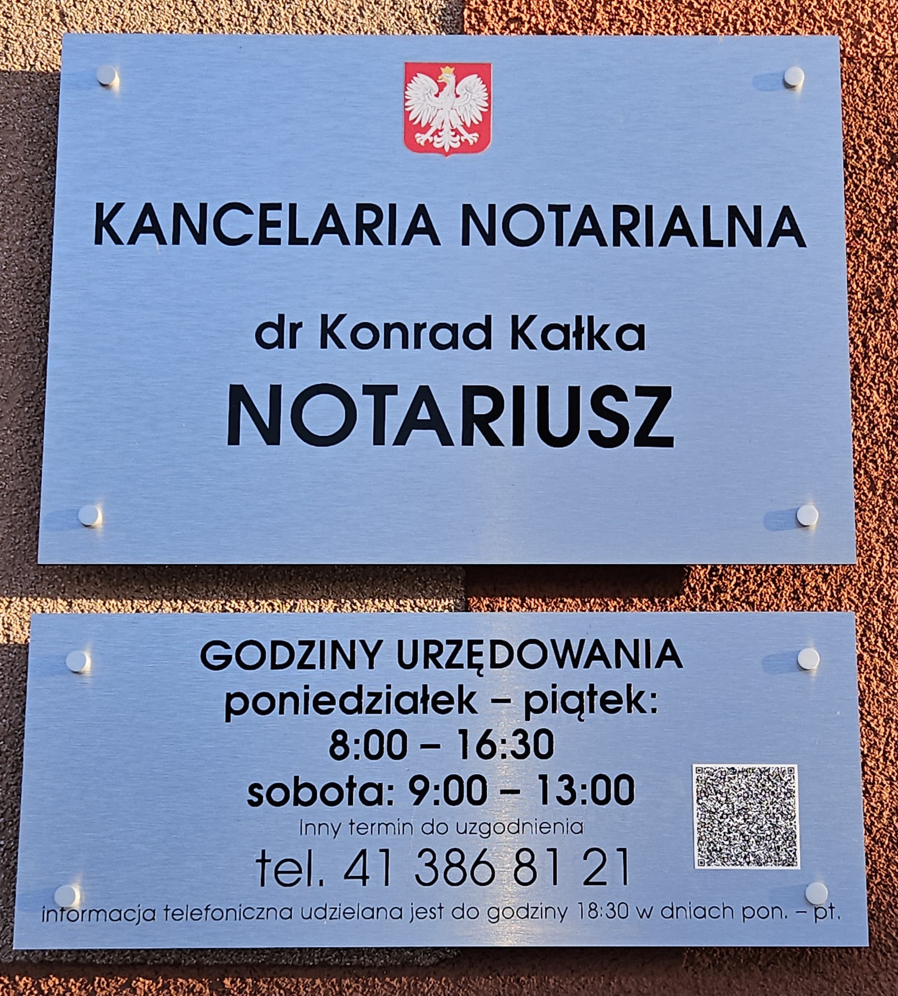 Tablica informacyjna na elewacji budynku z napisem 'Kancelaria Notarialna dr Konrad Kałka NOTARIUSZ', godłem Polski i godzinami urzędowania.