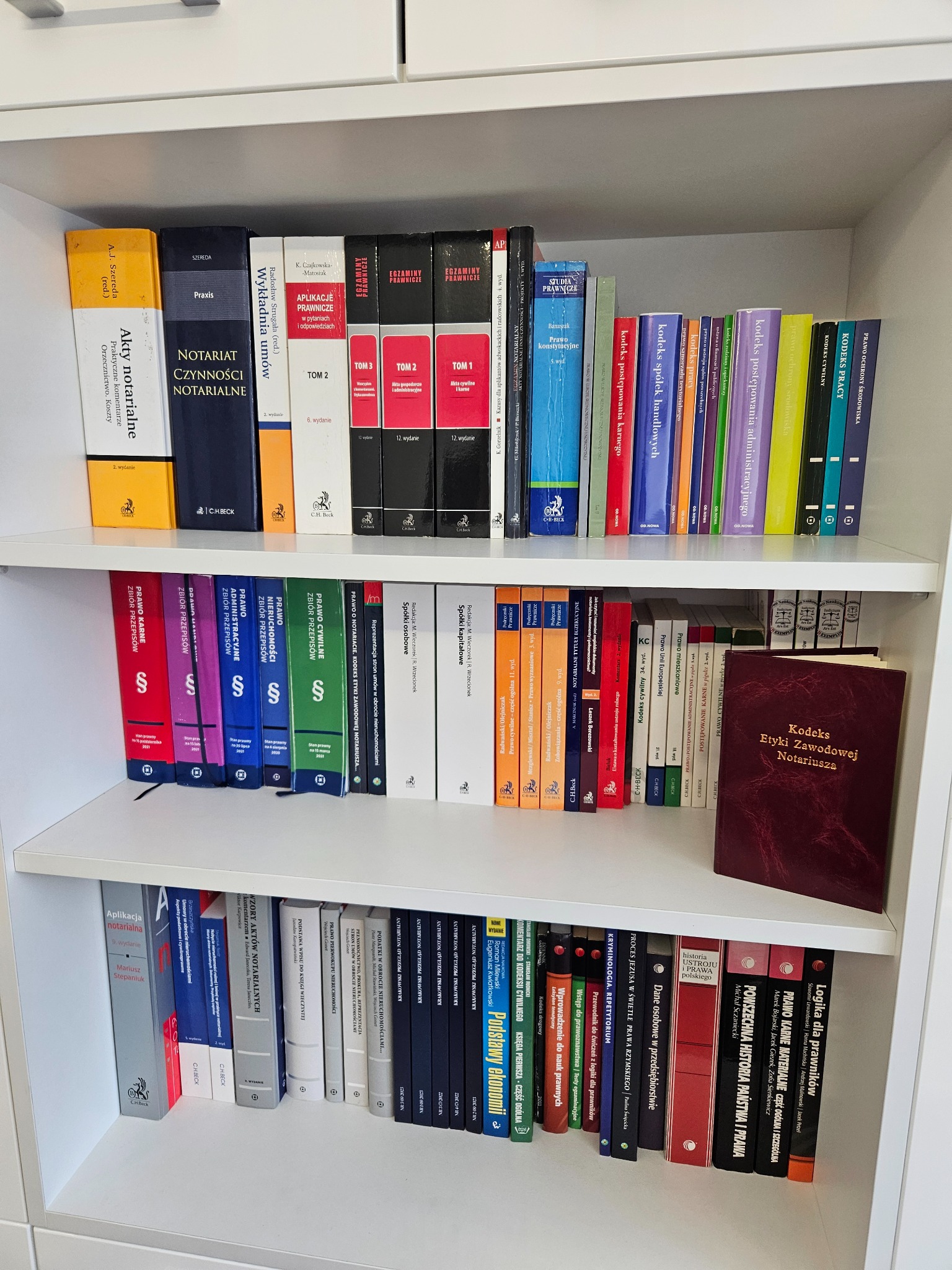 Półka z książkami prawniczymi, w tym kodeksy, komentarze i podręczniki, z wyraźnie widocznym tytułem 'Kodeks Etyki Zawodowej Notariusza' w dolnej części kadru.