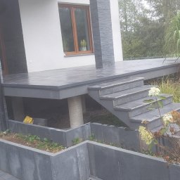 Firma Remontowo Budowlana Mariusz Kondracki - Szara, nowoczesna elewacja domu z tarasem, schodami i betonowymi donicami z roślinami, widok z góry na fragment elewacji.