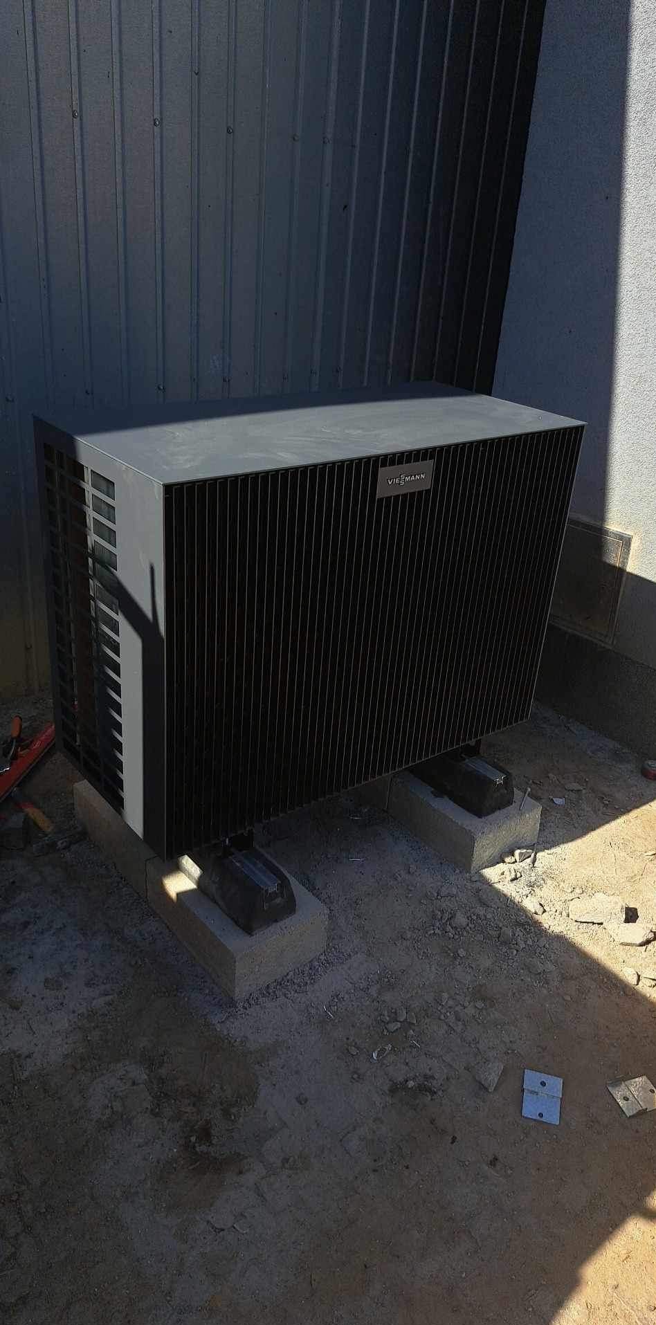Szary piec gazowy marki Viessmann, zamontowany na betonowych podstawach na zewnątrz budynku, widoczne narzędzia w tle.