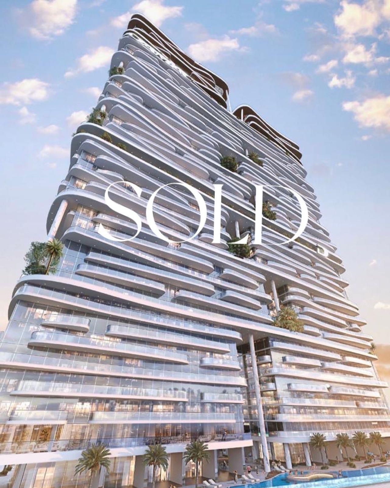 Wizualizacja nowoczesnego, wielopiętrowego apartamentowca z balkonami o falistym kształcie i napisem SOLD nałożonym na budynek, widok z dołu na tle błękitnego nieba.