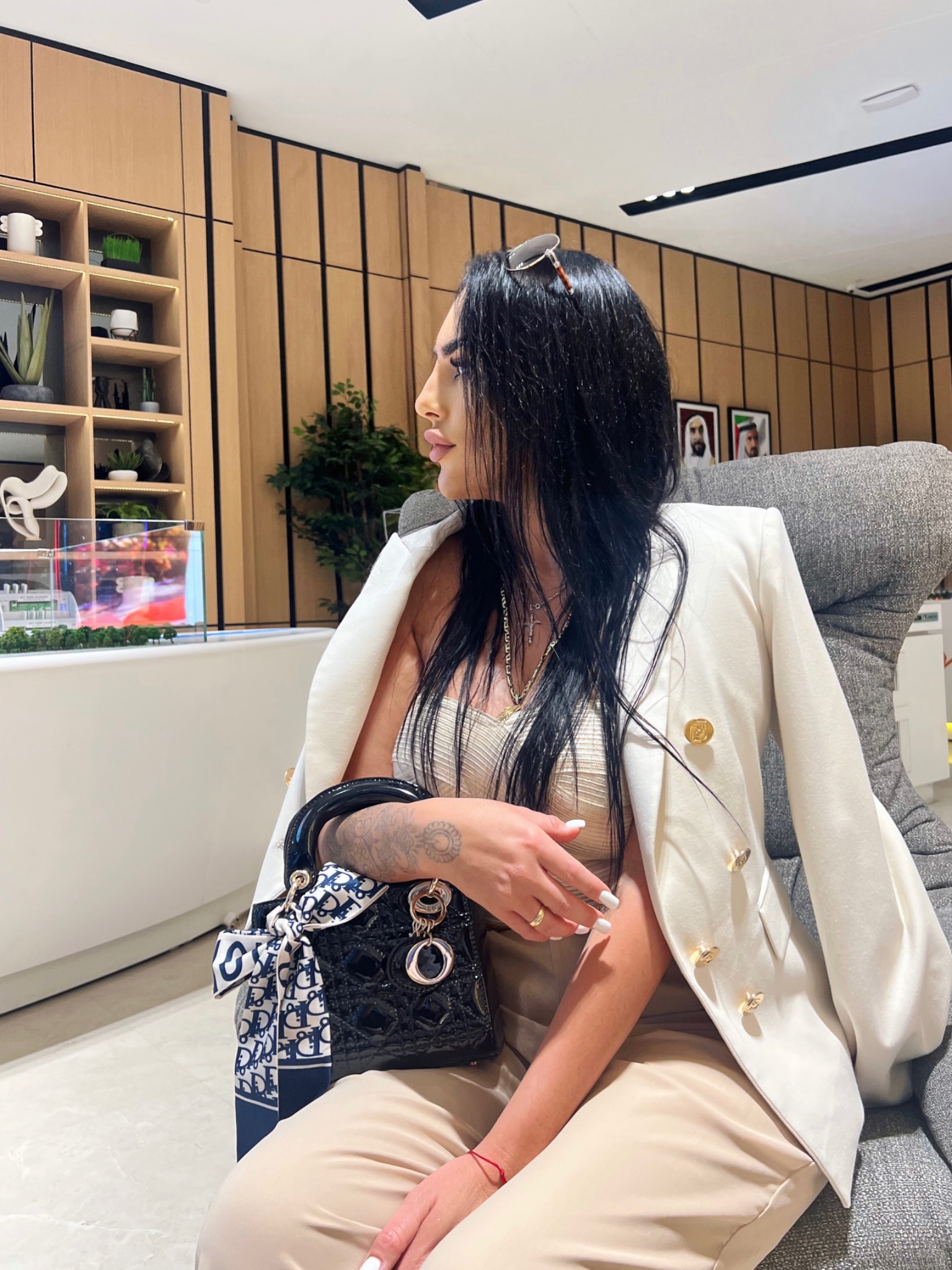 Kobieta w białym żakiecie siedzi w biurze nieruchomości, w tle model architektoniczny budynku.