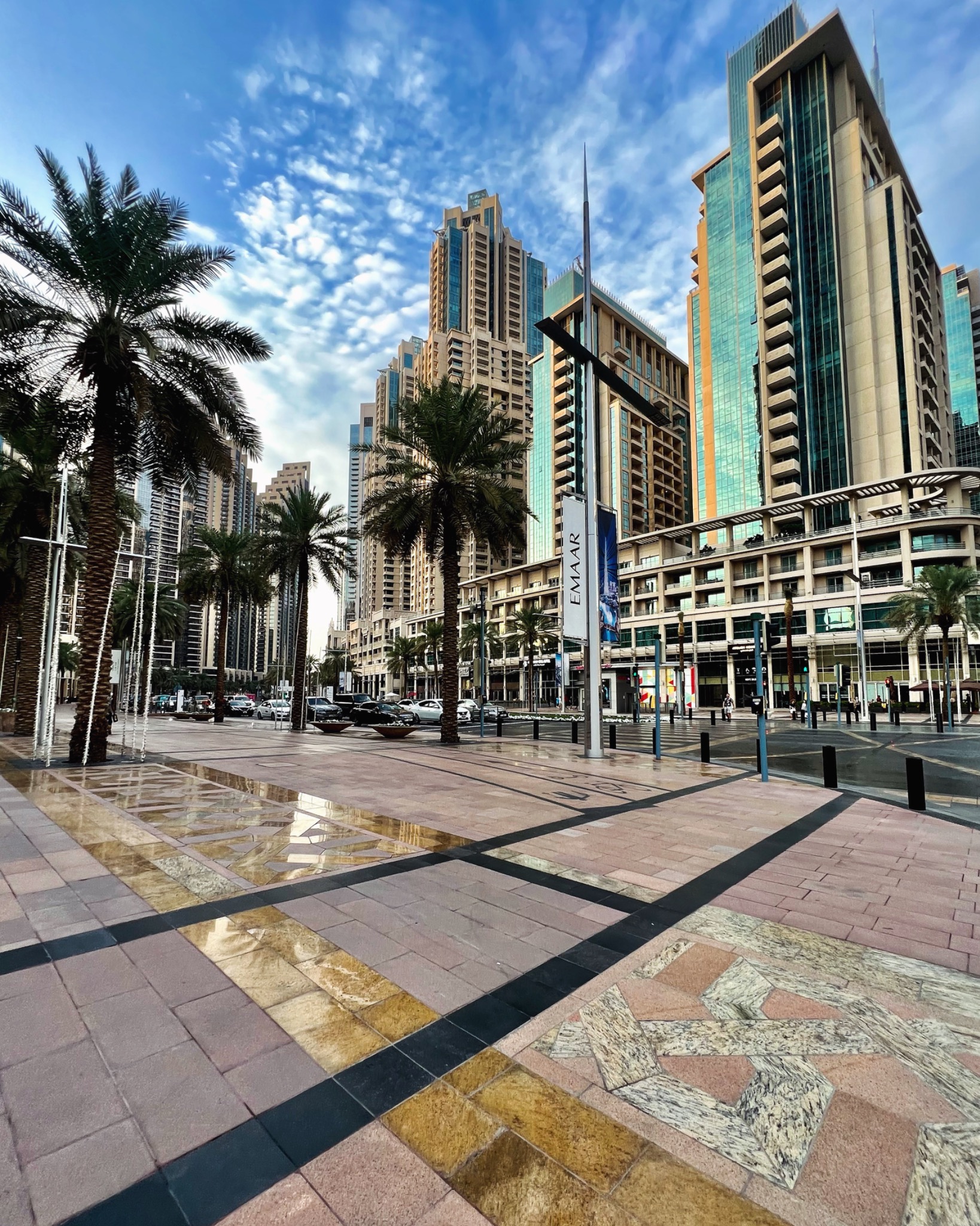 Panorama miasta z wysokimi budynkami, palmami i dekoracyjną nawierzchnią chodnika z refleksami wody