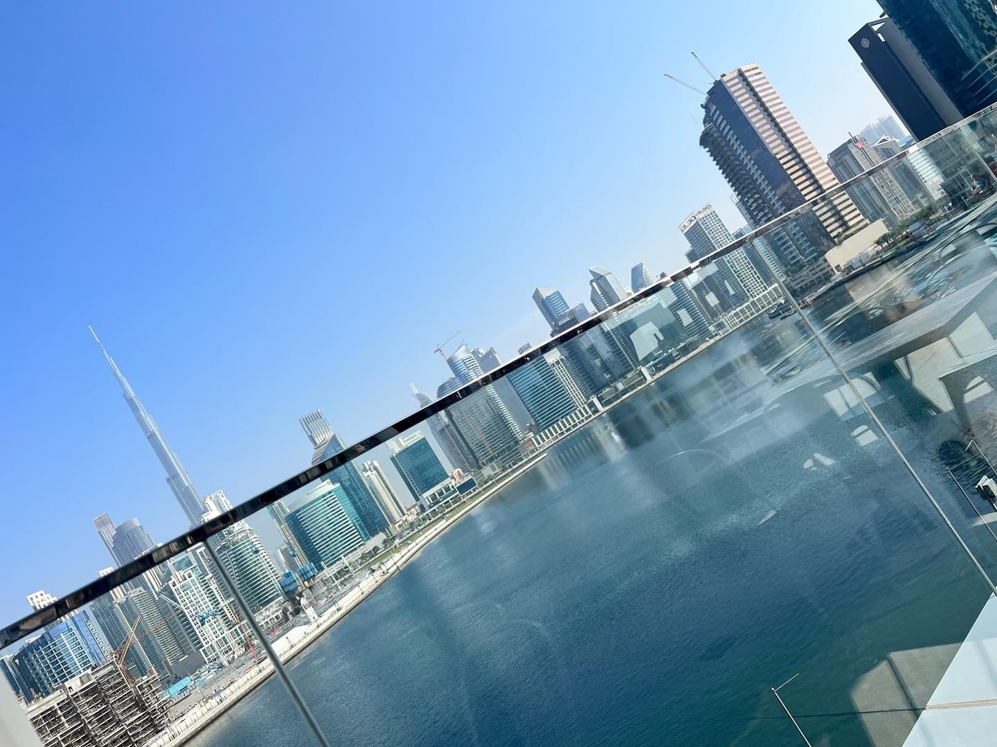 Panoramiczny widok na panoramę Dubaju z Burj Khalifa, widziany z balkonu z szklaną balustradą, odbijający się w wodzie kanału.