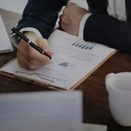 Mężczyzna w garniturze analizuje plan finansowy z wykresami na drewnianym biurku, obok laptopa i kubka.