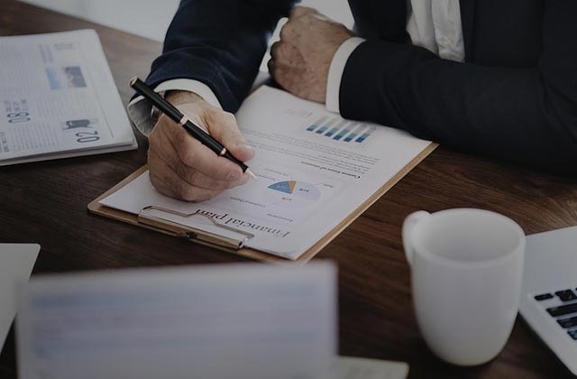 Mężczyzna w garniturze analizuje plan finansowy z wykresami na drewnianym biurku, obok laptopa i kubka.