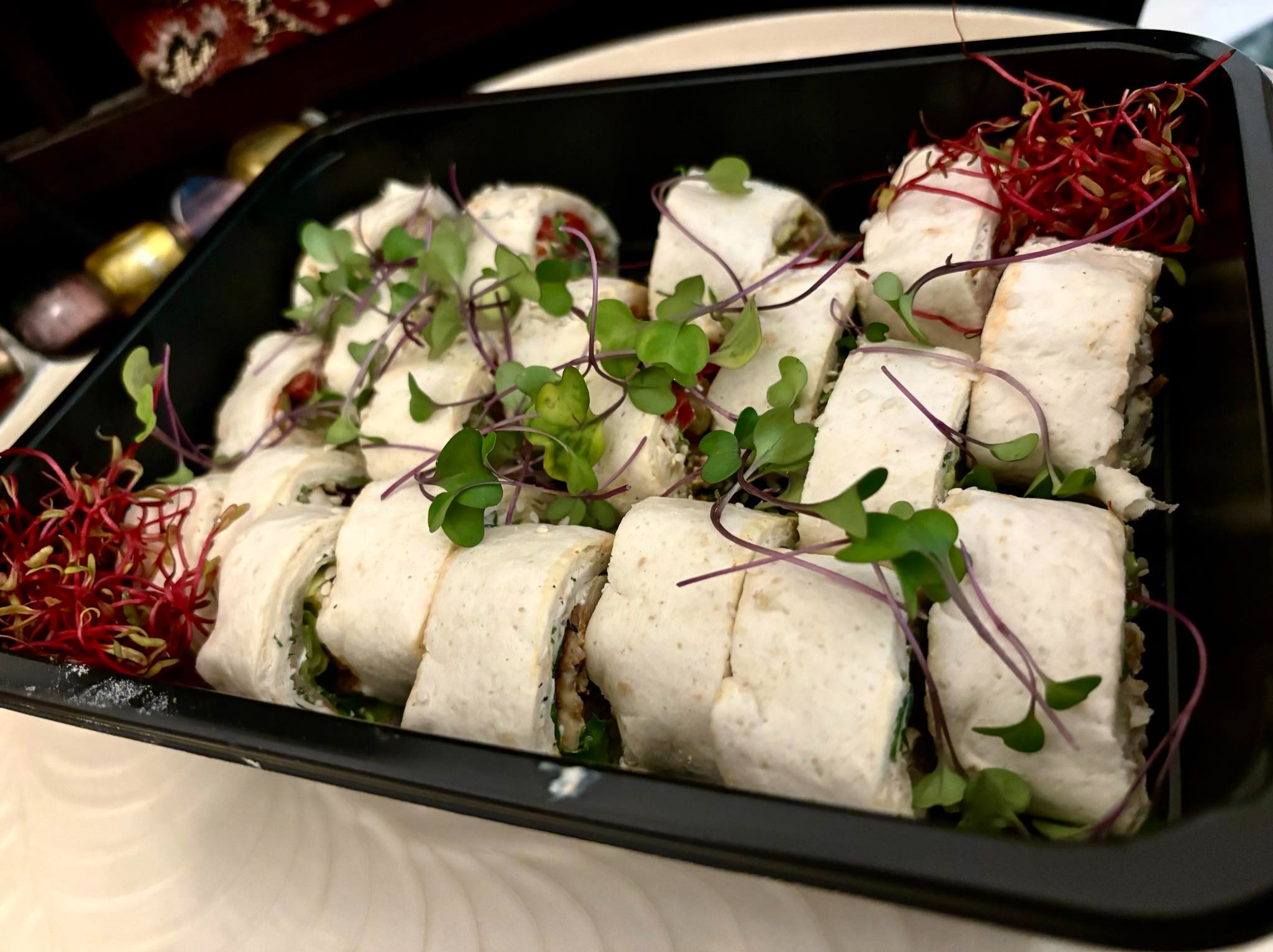 Tortilla wraps pokrojone w plastry, ułożone w czarnym pojemniku, udekorowane zielonymi i czerwonymi mikrolistkami.