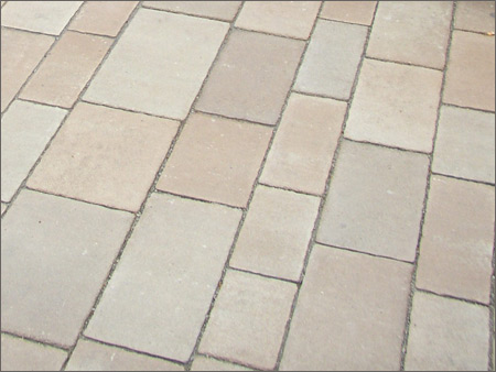 Ułożona nawierzchnia z prostokątnych płyt chodnikowych w odcieniach beżu i brązu, widoczna pod kątem, z delikatnymi szczelinami wypełnionymi piaskiem.