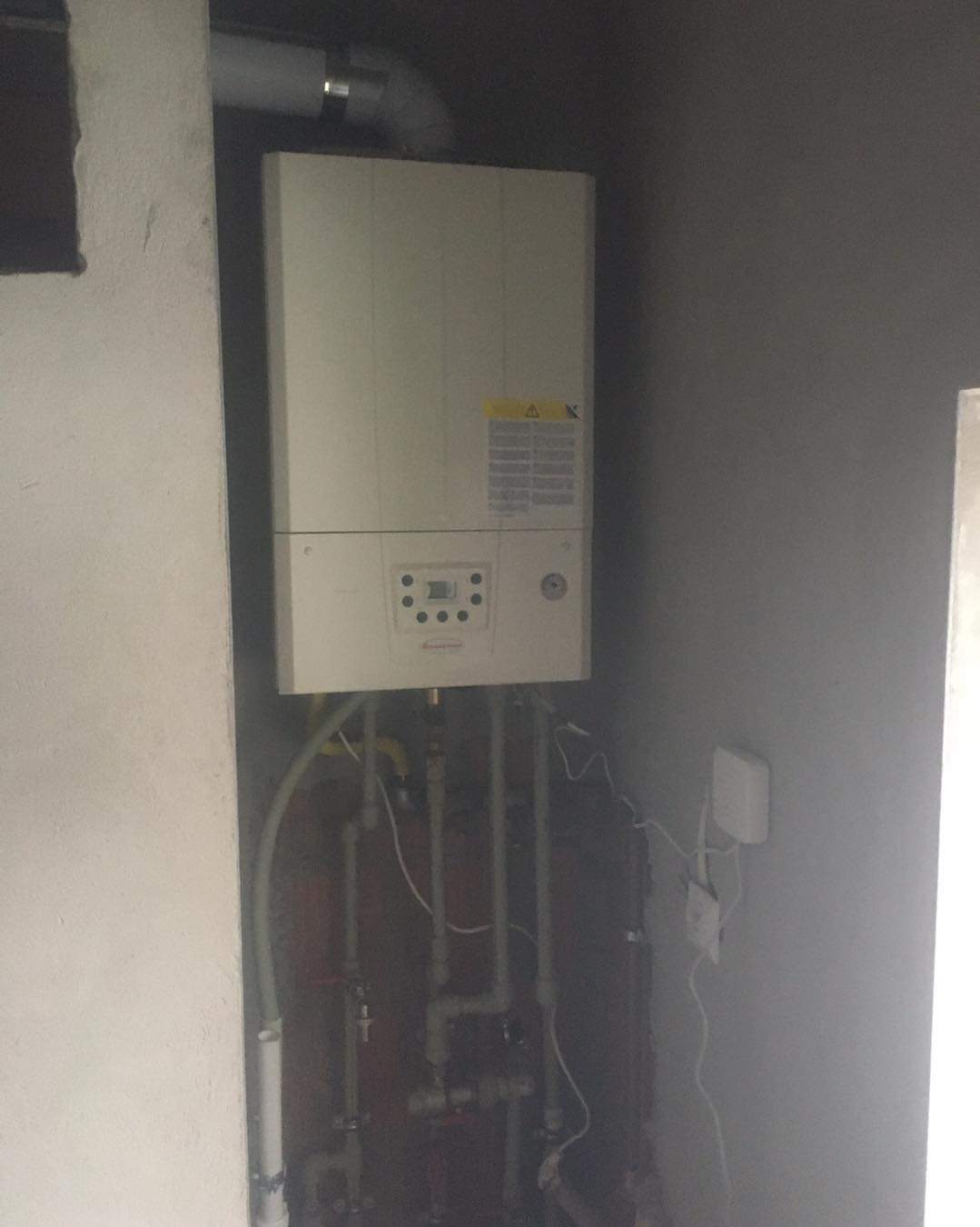 Zamontowany piec gazowy Ariston w surowym pomieszczeniu z widocznymi rurami instalacji hydraulicznej i przewodami elektrycznymi.