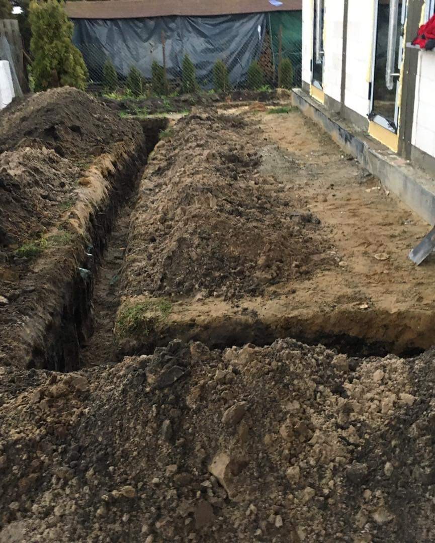 Wykop pod fundamenty domu jednorodzinnego, widoczne rowy w ziemi i pryzmy ziemi, przygotowanie terenu pod budowę.