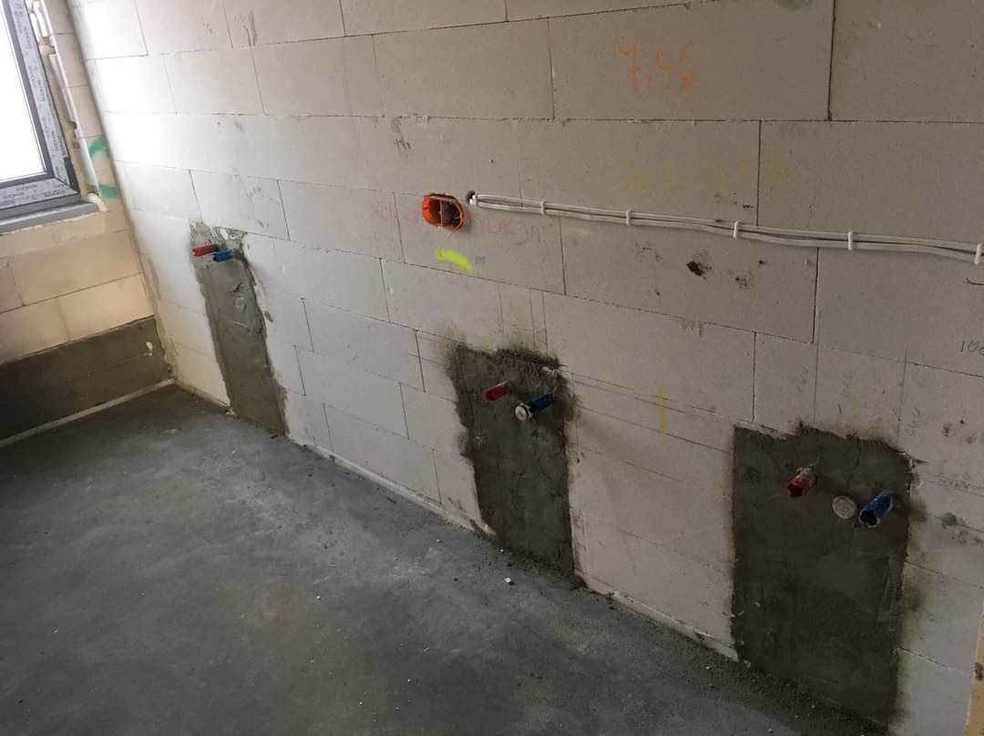 Przygotowanie do instalacji hydraulicznej w Zgierzu: ściana z betonu komórkowego z trzema punktami wyprowadzenia rur, zamurowane bruzdy, widoczne kable elektryczne i puszka instalacyjna.
