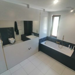 Dariusz Łokietek - Nowoczesna łazienka po remoncie z białą armaturą, płytkami podłogowymi w jasnym odcieniu i dużym lustrem z widocznym odbiciem toalety.