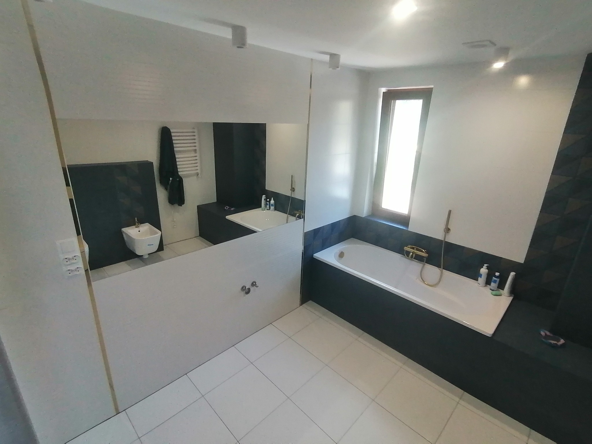 Nowoczesna łazienka po remoncie z białą armaturą, płytkami podłogowymi w jasnym odcieniu i dużym lustrem z widocznym odbiciem toalety.