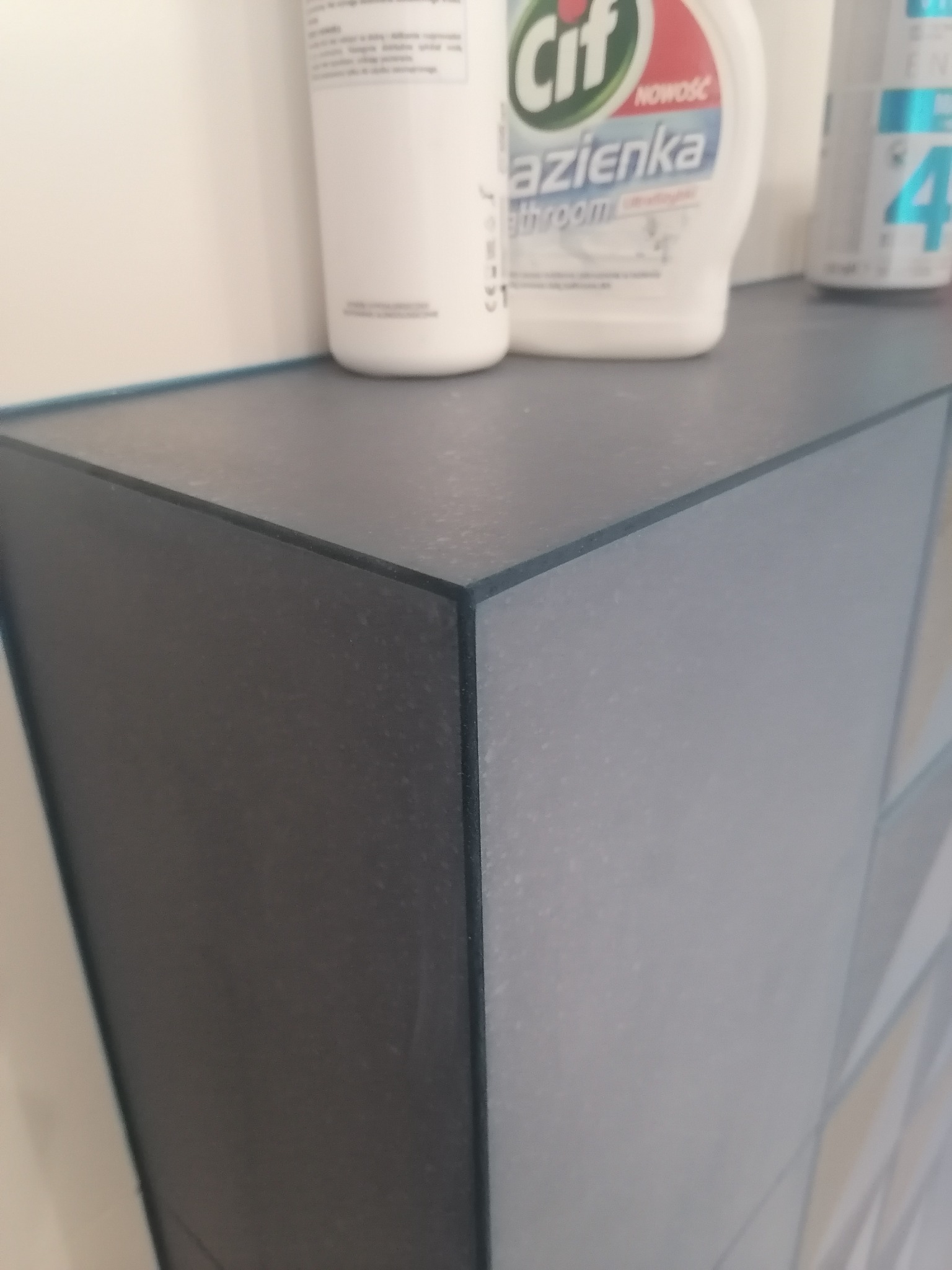 Szary narożny blat szafki łazienkowej z widocznymi środkami czystości, w tym butelką Cif do łazienek.