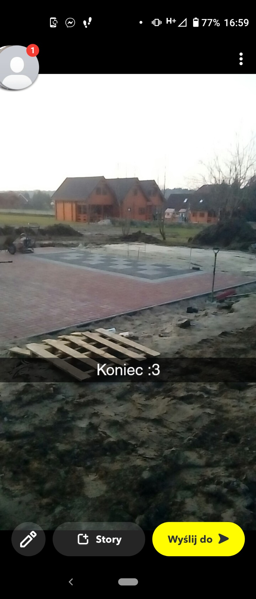 Częściowo ułożona, wzorzysta nawierzchnia z kostki brukowej na placu budowy, z widocznymi paletami i domami w tle, uchwycona w pochmurny dzień.