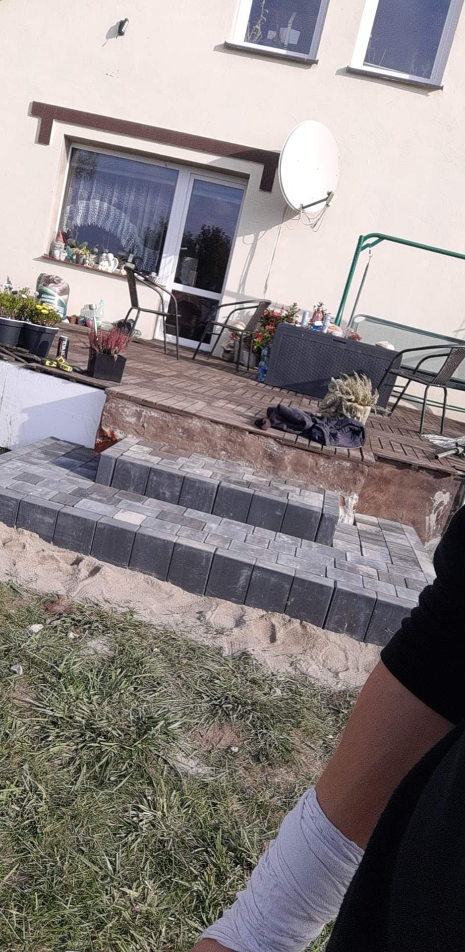 Schody z kostki brukowej prowadzące na drewniany taras przed domem, widoczne świeże ułożenie na podsypce piaskowej.