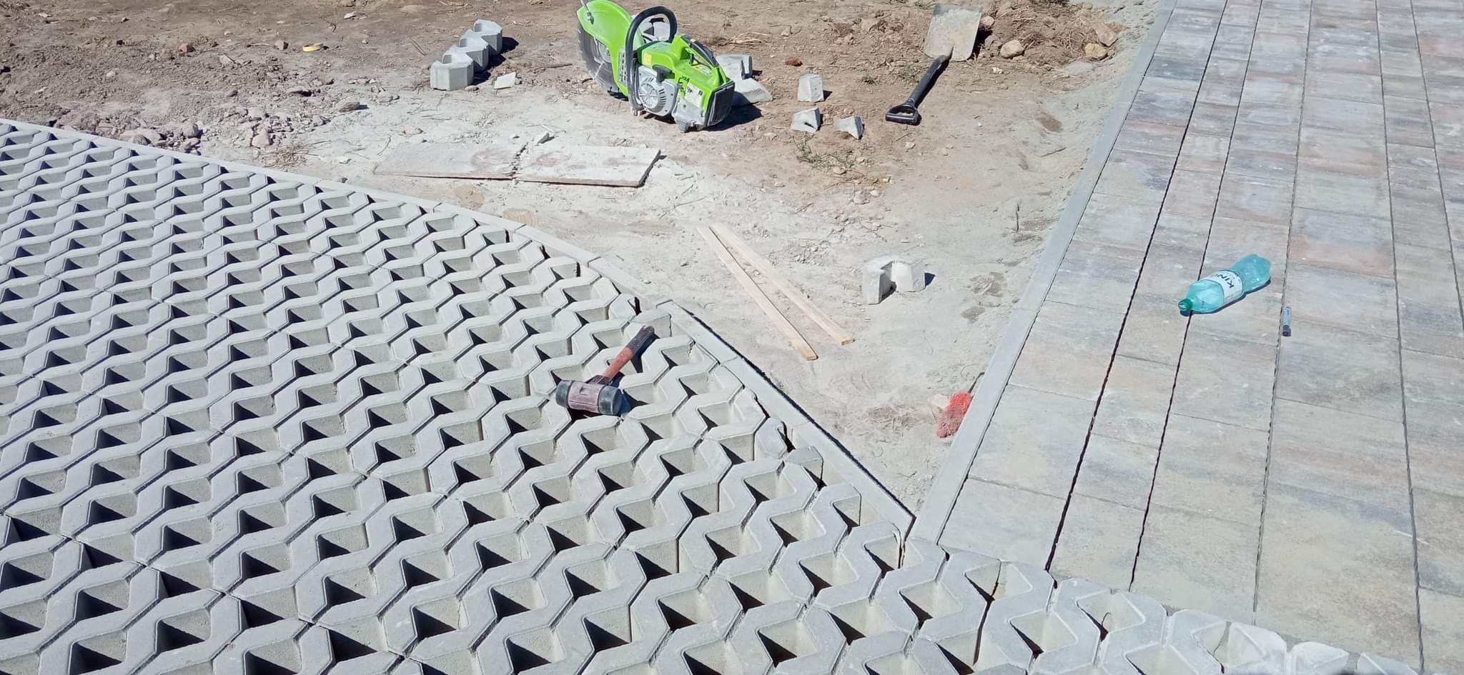 Fragment budowy nawierzchni z ażurowych płyt betonowych, widoczna piła do cięcia betonu, gumowy młotek i butelka wody.