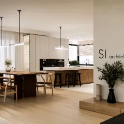 Jasne wnętrze domu z drewnianym stołem, krzesłami, wyspą kuchenną i minimalistycznym oświetleniem, uzupełnione roślinami i dekoracjami, z logo architektonicznym w prawym górnym rogu.