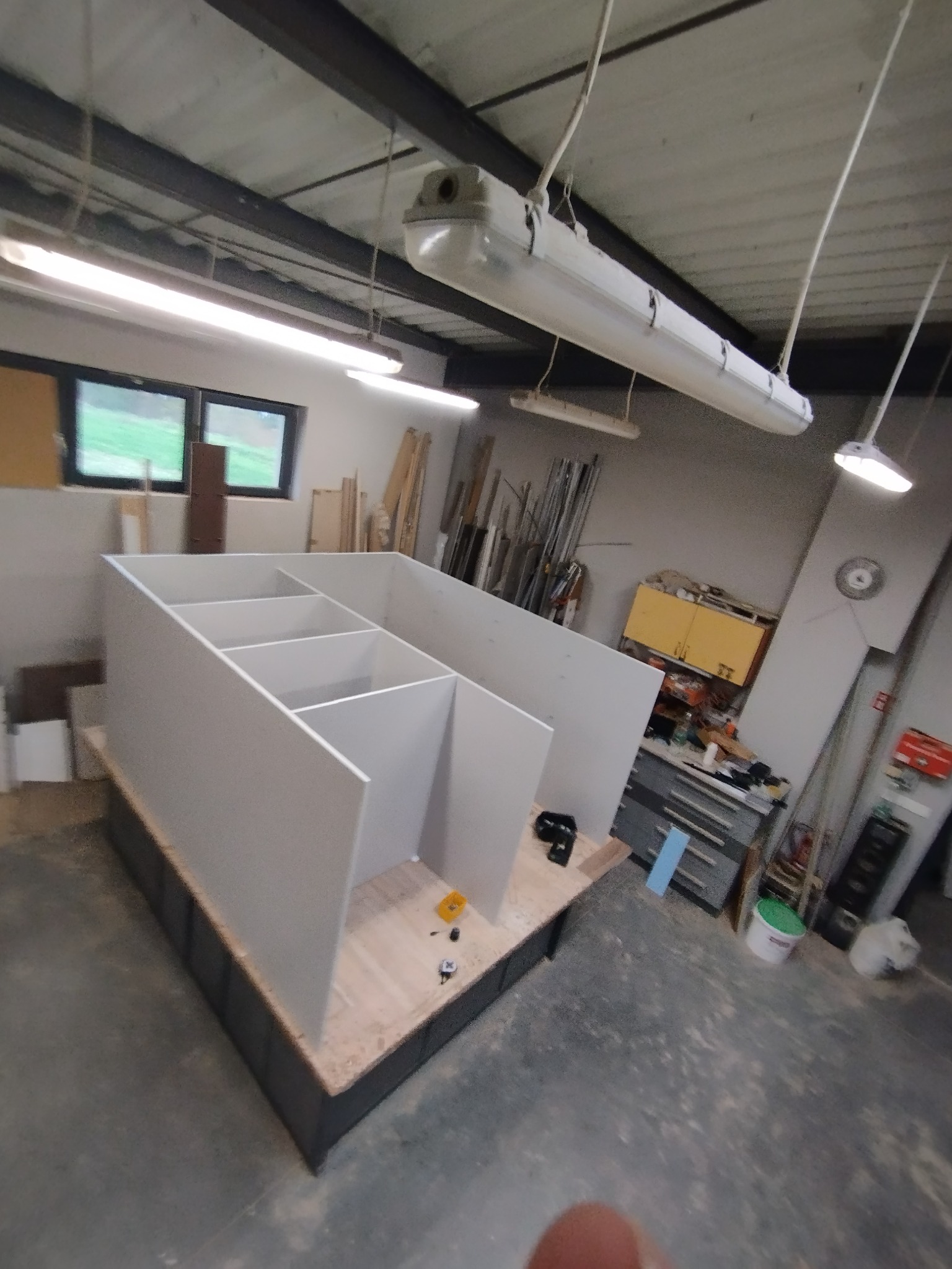 Wnętrze warsztatu z widoczną konstrukcją szafy wnękowej w trakcie montażu, widoczne elementy mocujące oraz narzędzia, w tle regały warsztatowe.