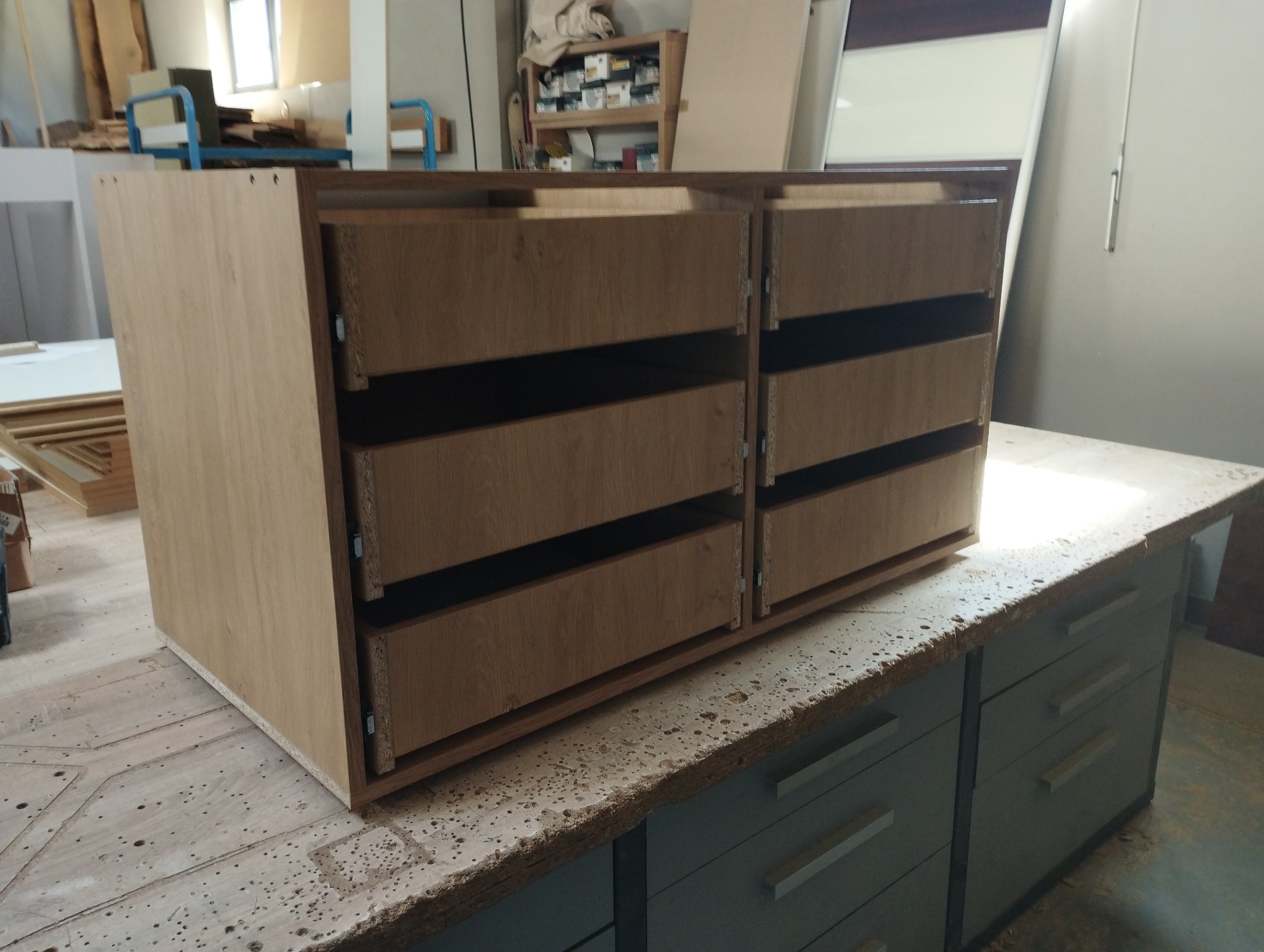 Szafka z jasnego drewna z sześcioma szufladami bez frontów, umieszczona na roboczym stole w warsztacie stolarskim.