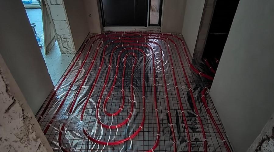 Czerwone rury ogrzewania podłogowego ułożone na siatce, widok z góry w surowym wnętrzu z oknem.