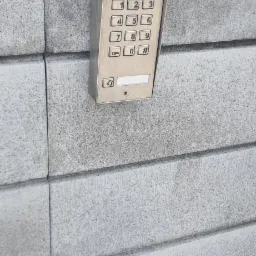 Zewnętrzny panel domofonowy ACO z klawiaturą numeryczną, zamontowany na szarym, betonowym murze.