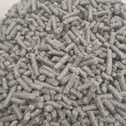 Stos szarego, szorstkiego pelletu z biomasy w jasnym pojemniku, widok z góry.