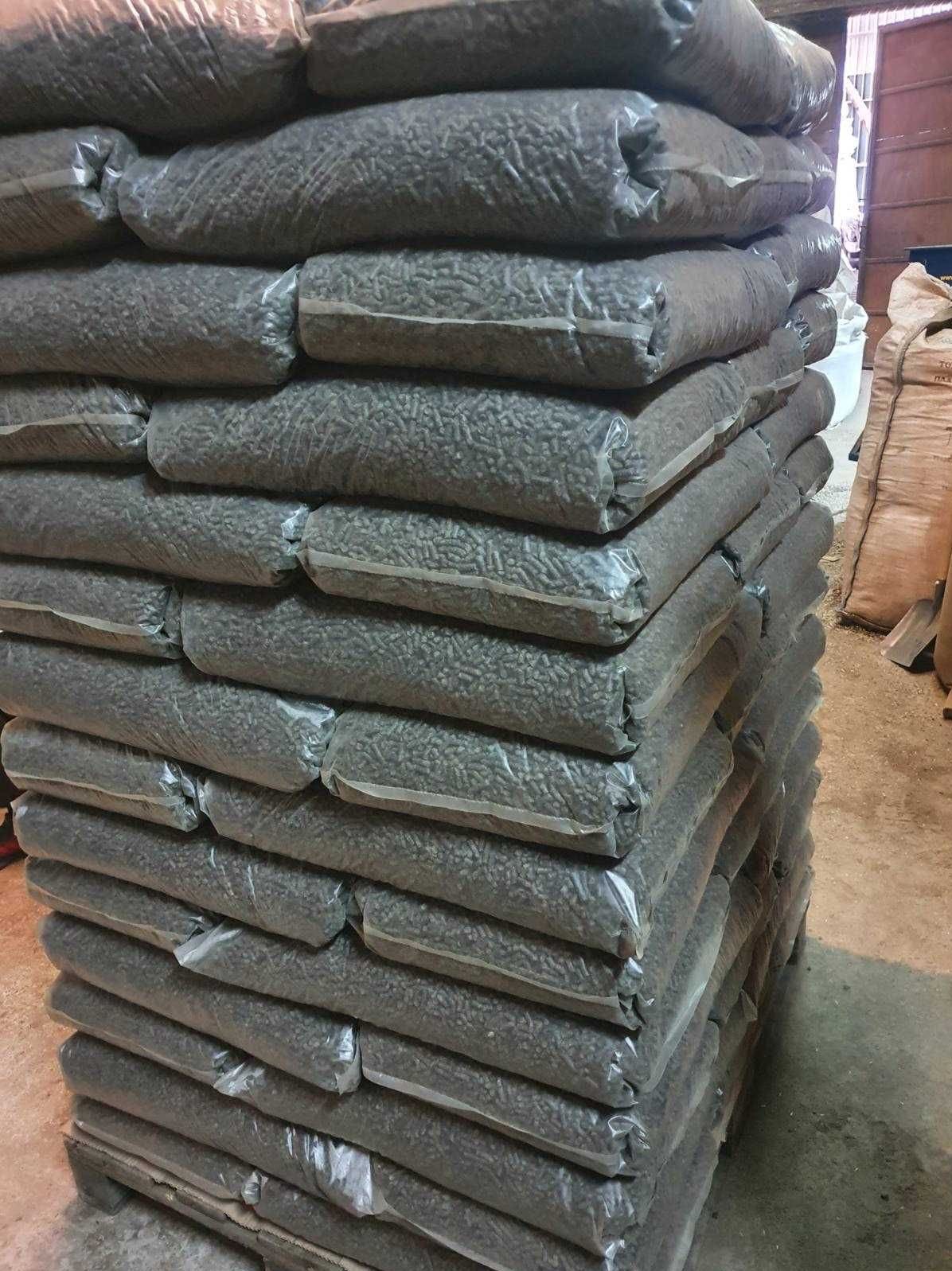 Stos worków z pelletem na palecie, widoczne szwy worków i struktura pelletu, tło magazynowe.