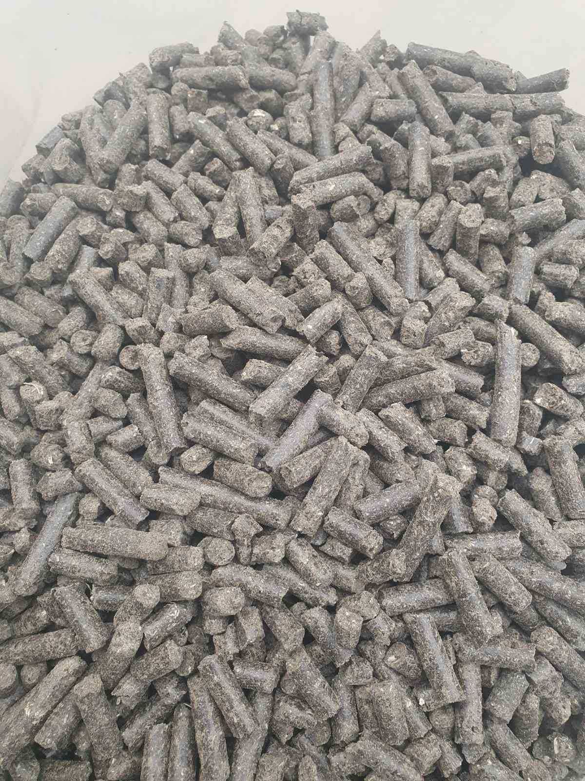 Stos szarego, szorstkiego pelletu z biomasy w jasnym pojemniku, widok z góry.