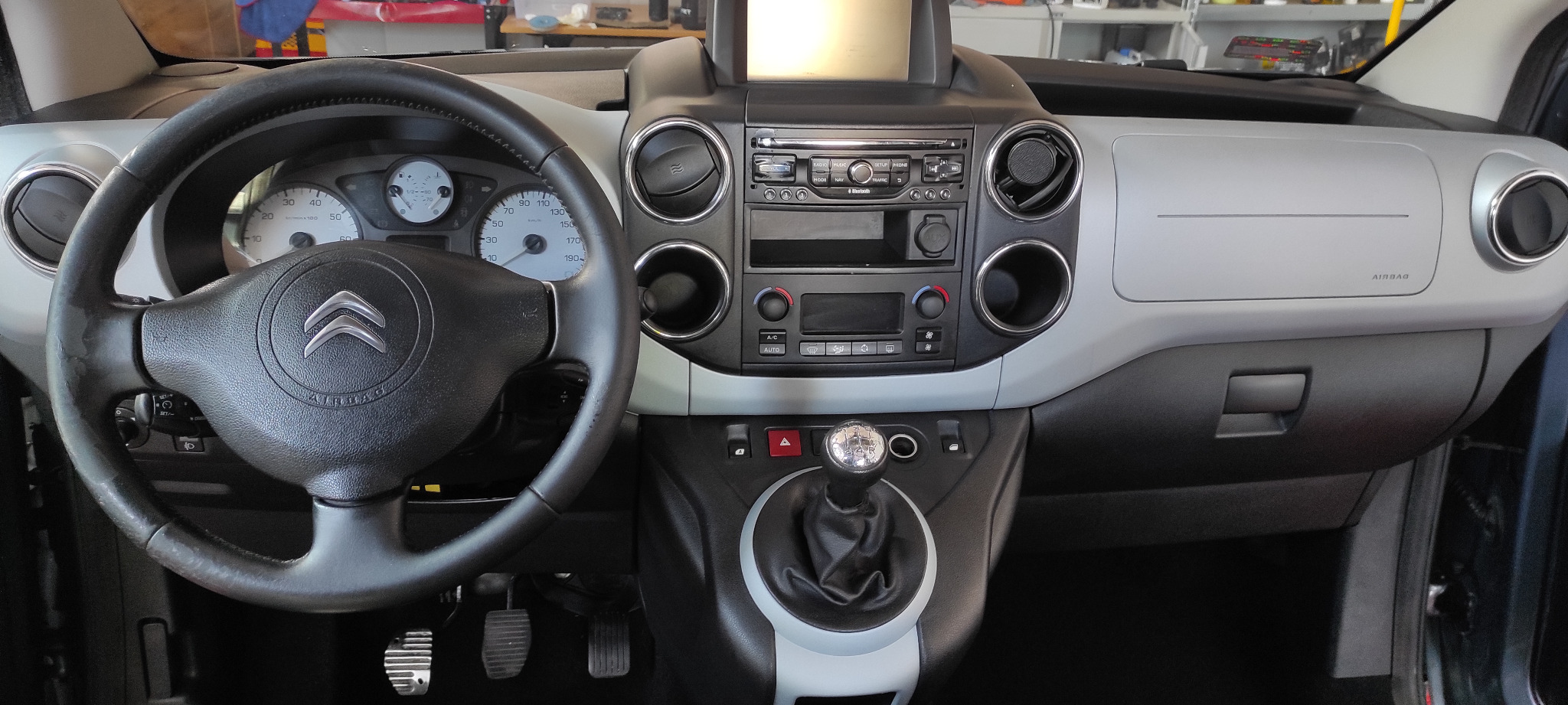 Wnętrze samochodu marki Citroen, widok na deskę rozdzielczą, kierownicę z logo, radio, nawiewy i dźwignię zmiany biegów.