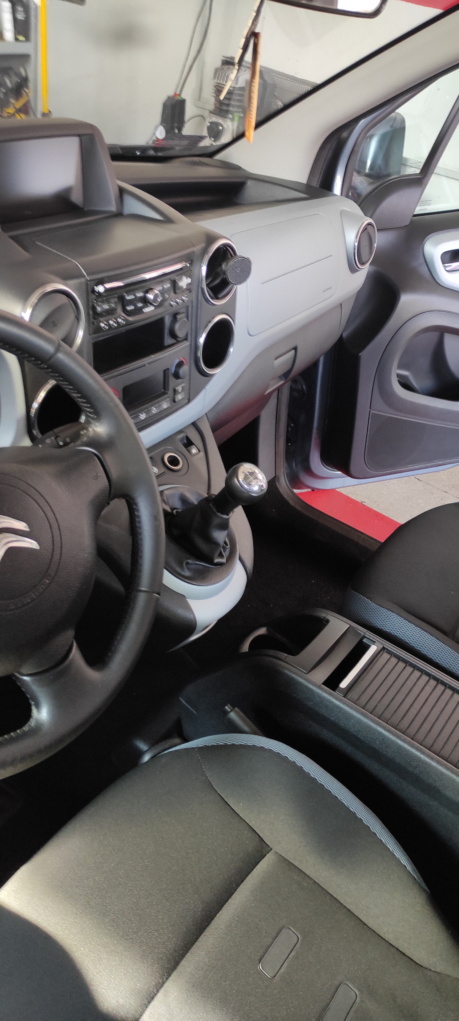 Wnętrze samochodu Citroen Berlingo z widoczną kierownicą, deską rozdzielczą i dźwignią zmiany biegów, ukazujące detale tapicerki i elementów wykończeniowych.