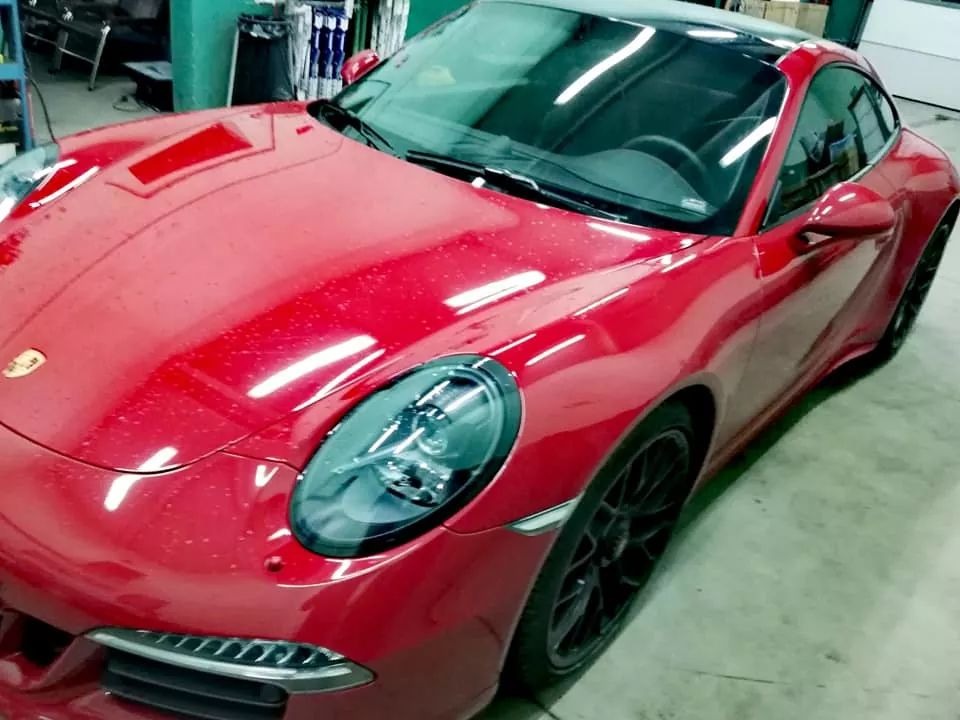 Czerwone Porsche 911 z czarnym dachem w warsztacie, widoczne drobne zabrudzenia na lakierze i odbicia światła, czarne felgi.