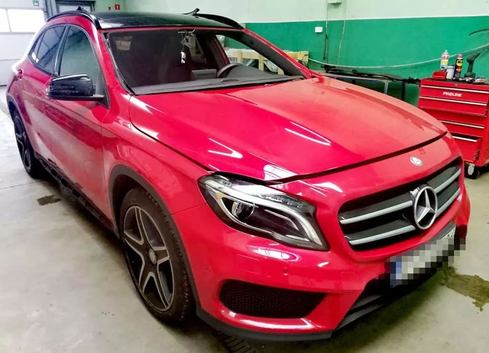 Czerwony Mercedes GLA z nową szybą przednią, zaparkowany w warsztacie samochodowym, widoczny wózek narzędziowy.