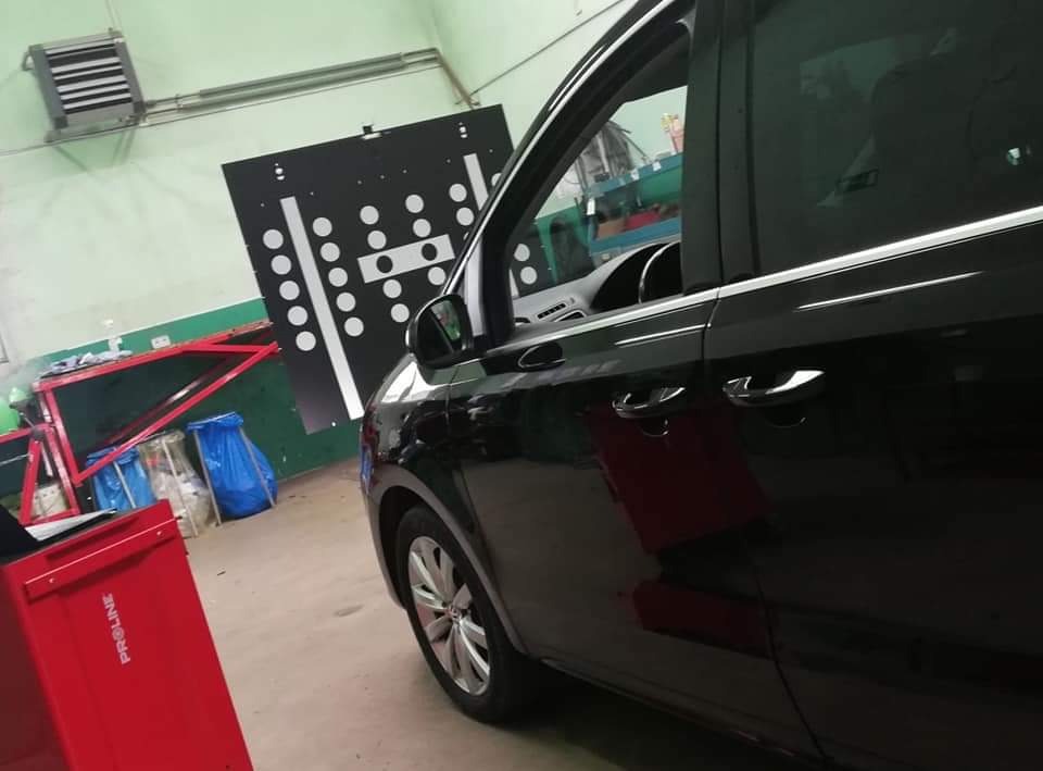 Czarny samochód osobowy na stanowisku do geometrii kół, widoczna tarcza pomiarowa i czerwona szafka urządzenia Proline.