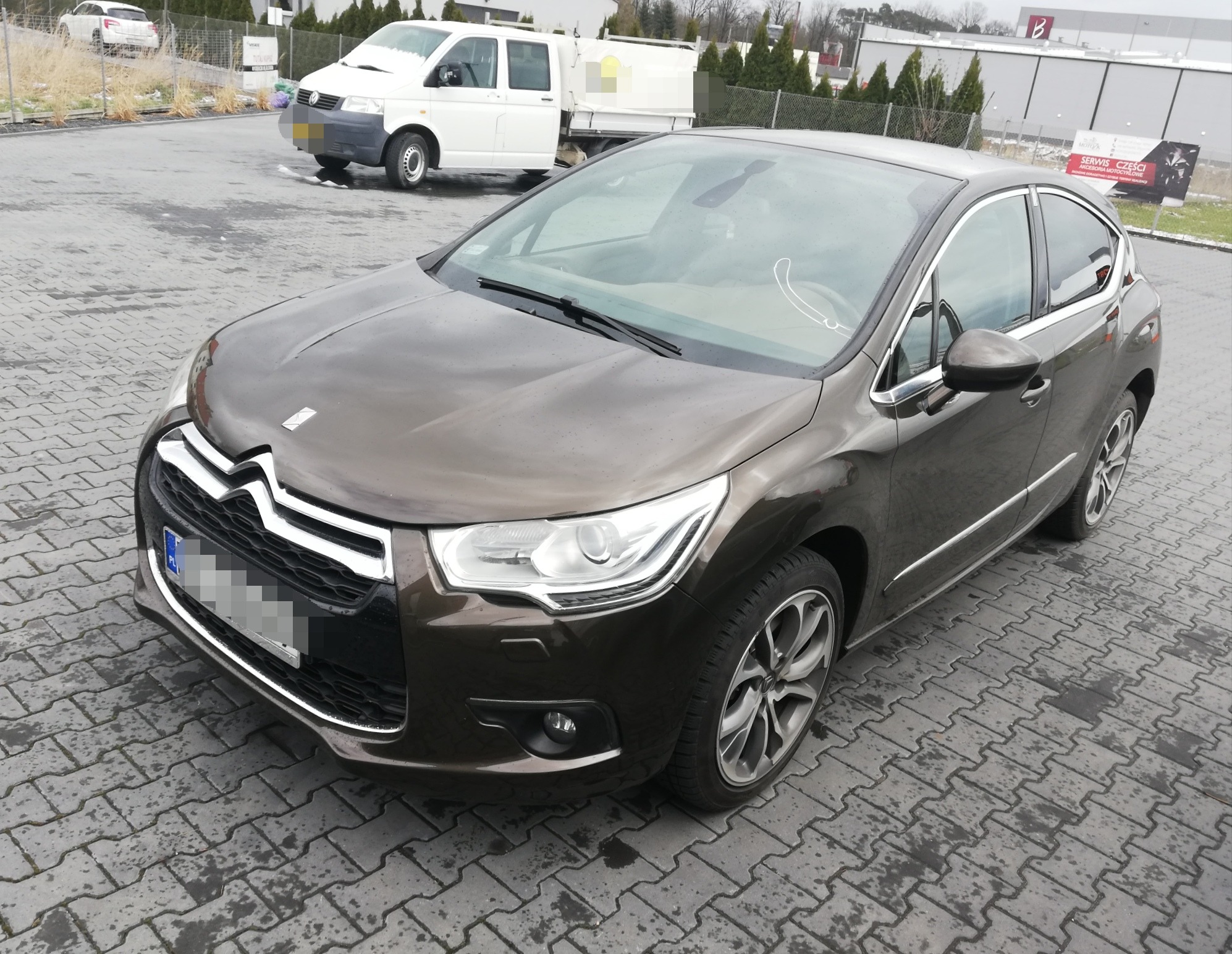 Brązowy Citroen DS4 zaparkowany na mokrej kostce brukowej, widok z przodu i z boku, na szybie widoczna przyssawka uchwytu.