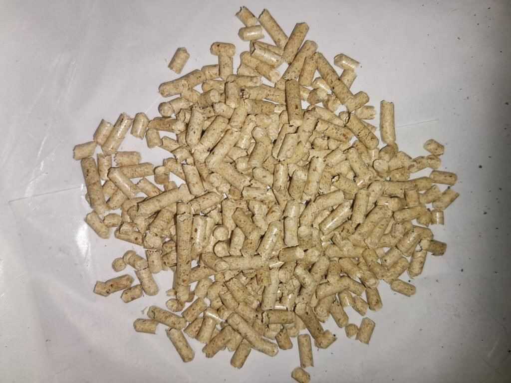 Jasny, beżowy pellet drzewny ułożony w kopiec na białym, lekko pofałdowanym podłożu.