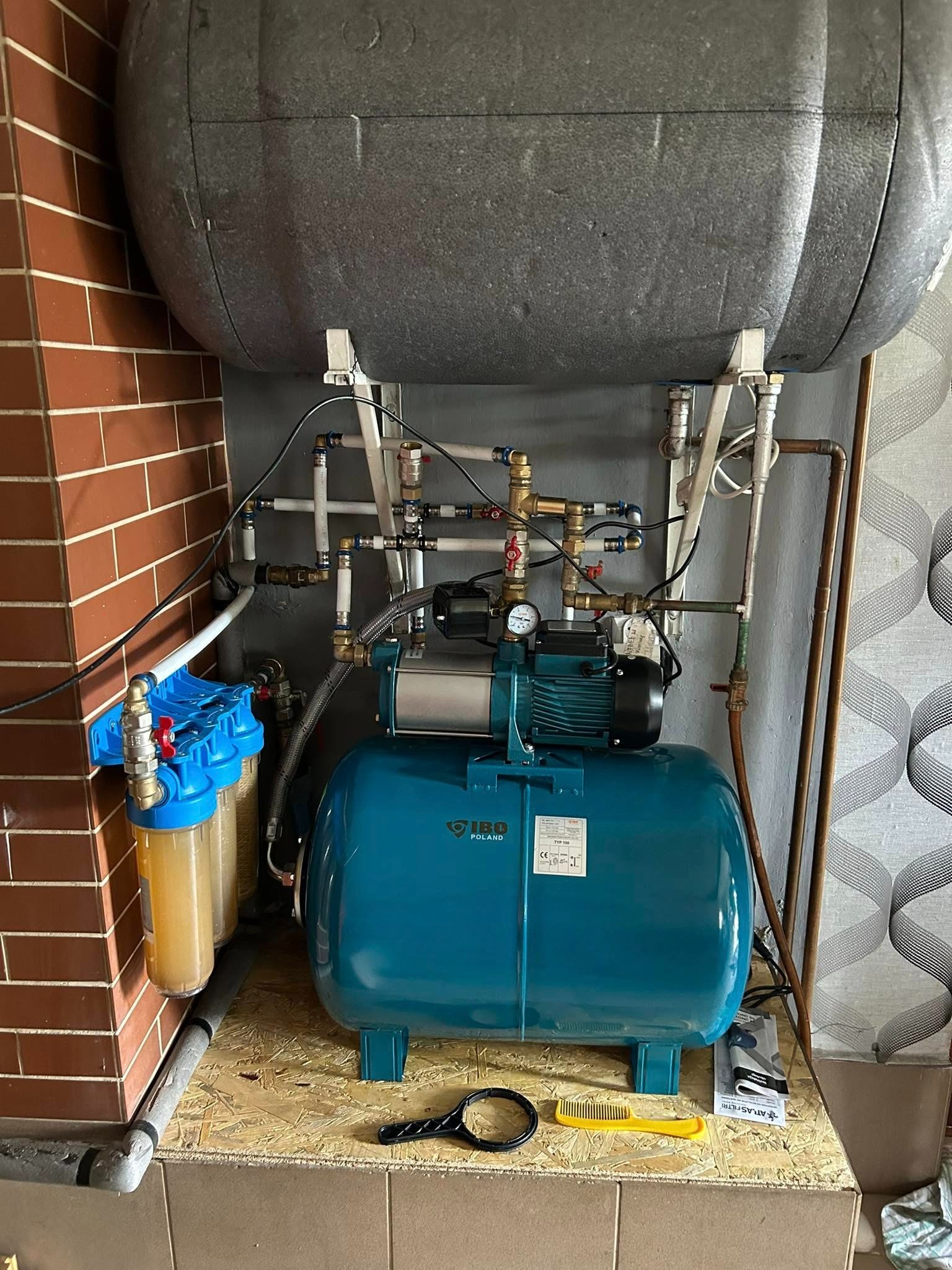Ukończona instalacja hydroforowa z filtrami wody, zbiornikiem akumulacyjnym i pompą, umieszczona na płycie OSB, z widocznymi rurami i armaturą.