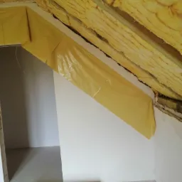 Ocieplanie poddasza wełną mineralną, zabezpieczoną folią paroizolacyjną, widoczny fragment ściany i podłogi w trakcie prac.