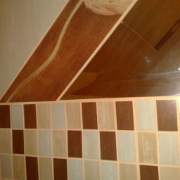 Robert Góra - Fragment ściany w łazience z dekoracyjnymi, brązowo-beżowymi płytkami ułożonymi w szachownicę i nietypową mozaiką na górze, z widoczną tubką kosmetyku na półce.