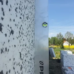 Sprawdzanie poziomu ściany ocieplonej styropianem z fakturą 'baranka' za pomocą poziomicy PRO ERS+ z 10-letnią gwarancją na wskaźniki, w tle teren budowy i błękitne niebo.