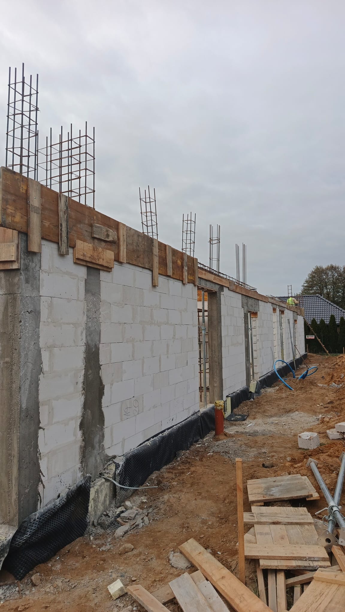 Budowa domu z betonu komórkowego w Ostrołęce. Widoczne ściany, zbrojenia i szalunki. Etap wznoszenia ścian parteru, zabezpieczenie przeciwwilgociowe fundamentów.