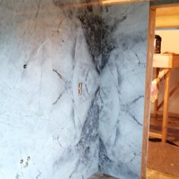 ProTejgels Adrian Dąbrowski - Wnętrze łazienki w trakcie remontu, ściany wykończone płytami imitującymi marmur, podłoga wyłożona heksagonalnymi płytkami, widoczne wystające kable i puszka elektryczna, drewniana konstrukcja...