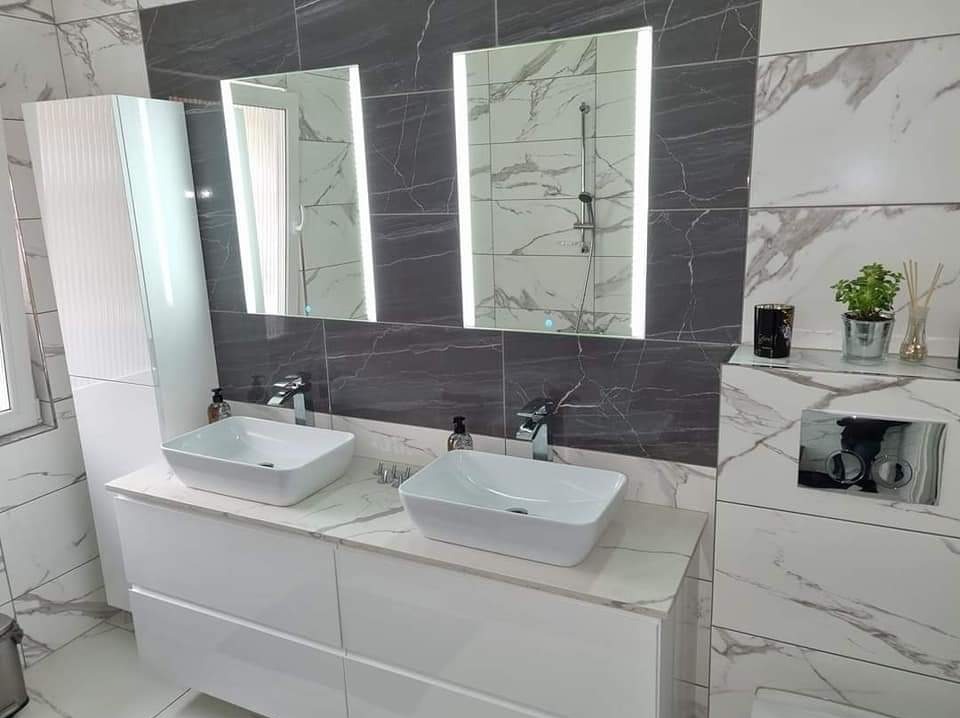 Nowoczesna łazienka z dwiema białymi umywalkami nablatowymi, podświetlanymi lustrami i marmurowymi płytkami w odcieniach szarości i bieli.