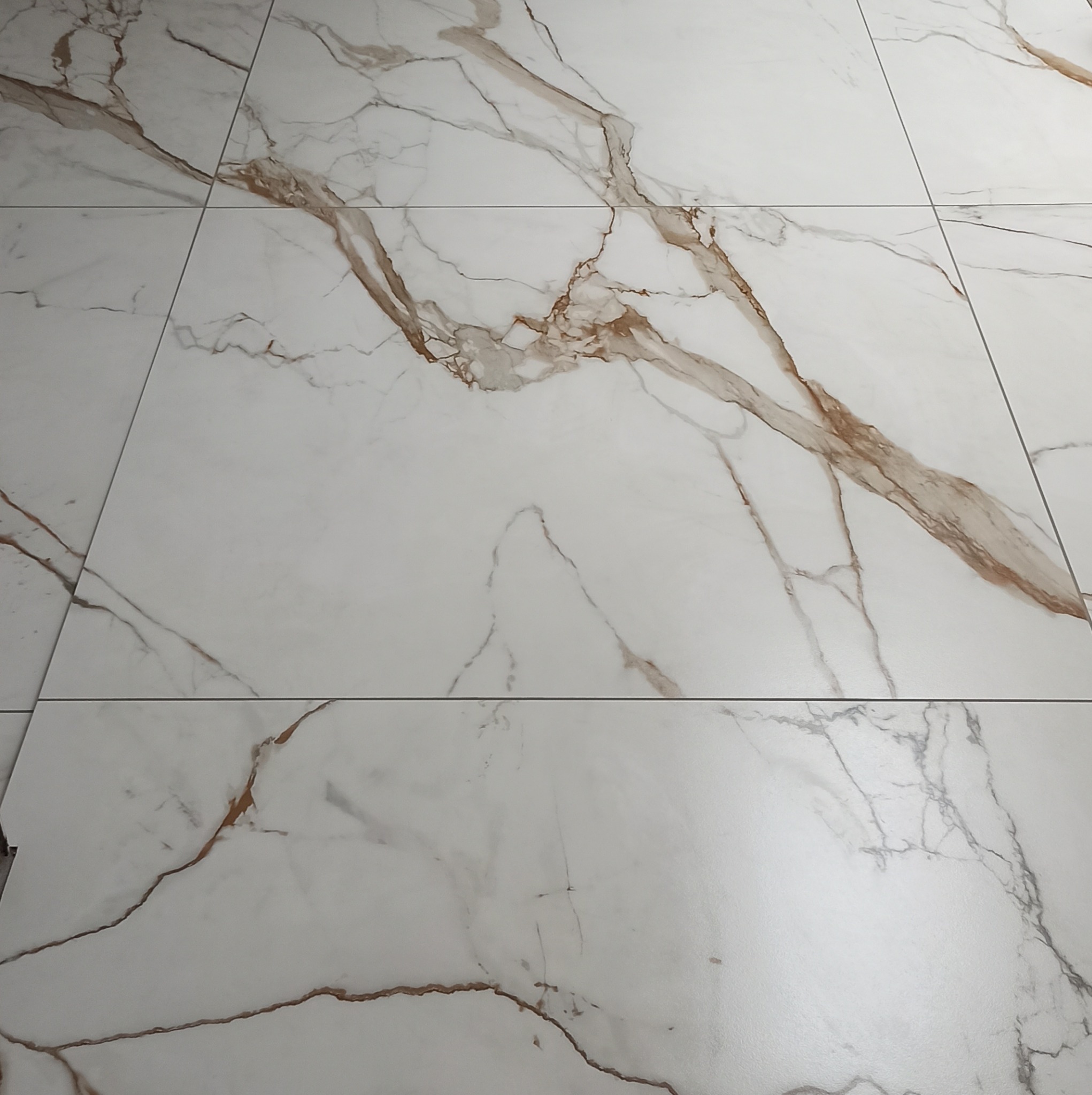 Ułożone płytki podłogowe z białego marmuru z brązowymi żyłami, widoczne fugi.