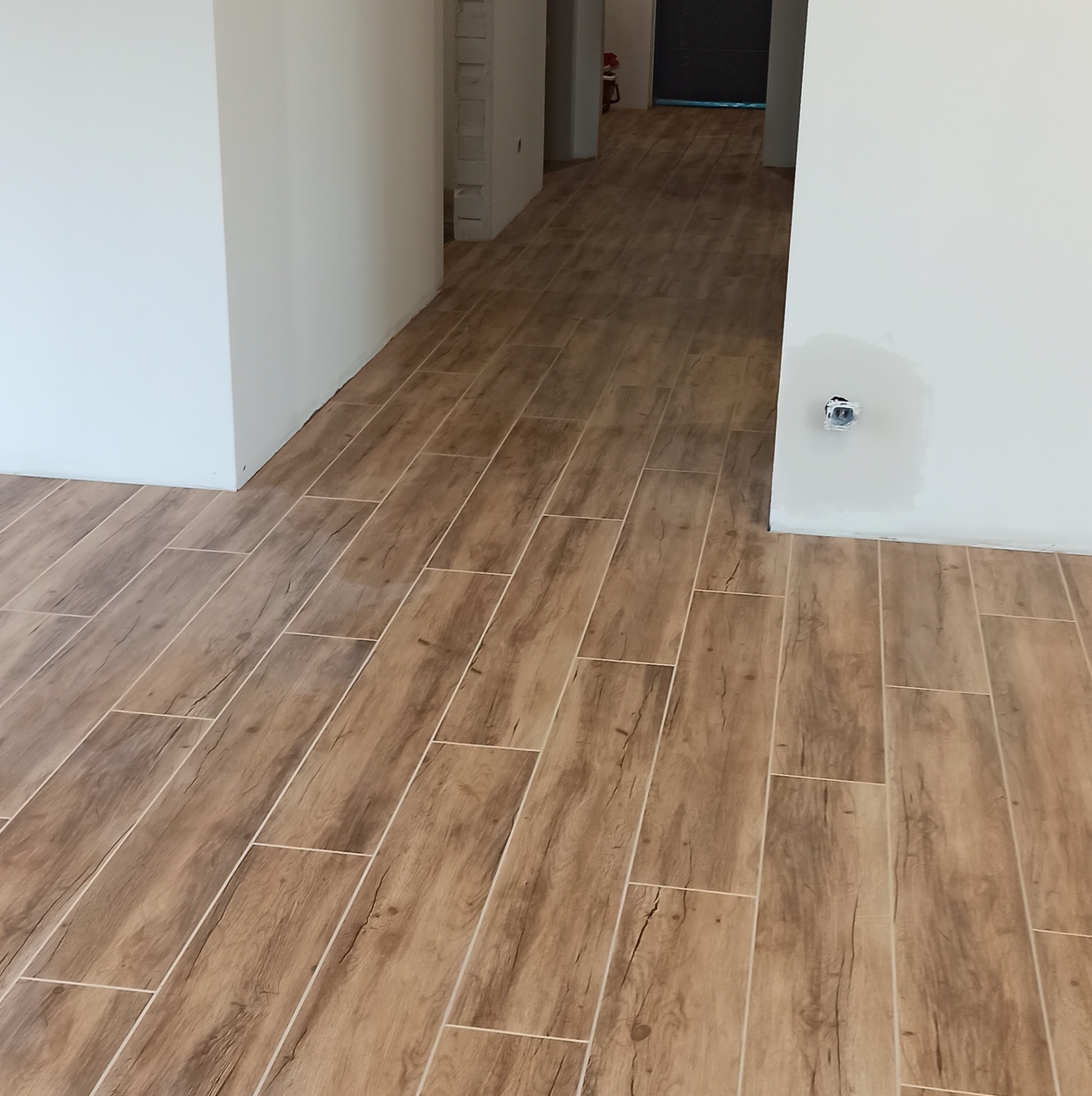 Ułożona podłoga z płytek imitujących drewno w korytarzu, ściany pomalowane na biało, widoczne niedokończone gładzie przy gniazdku.