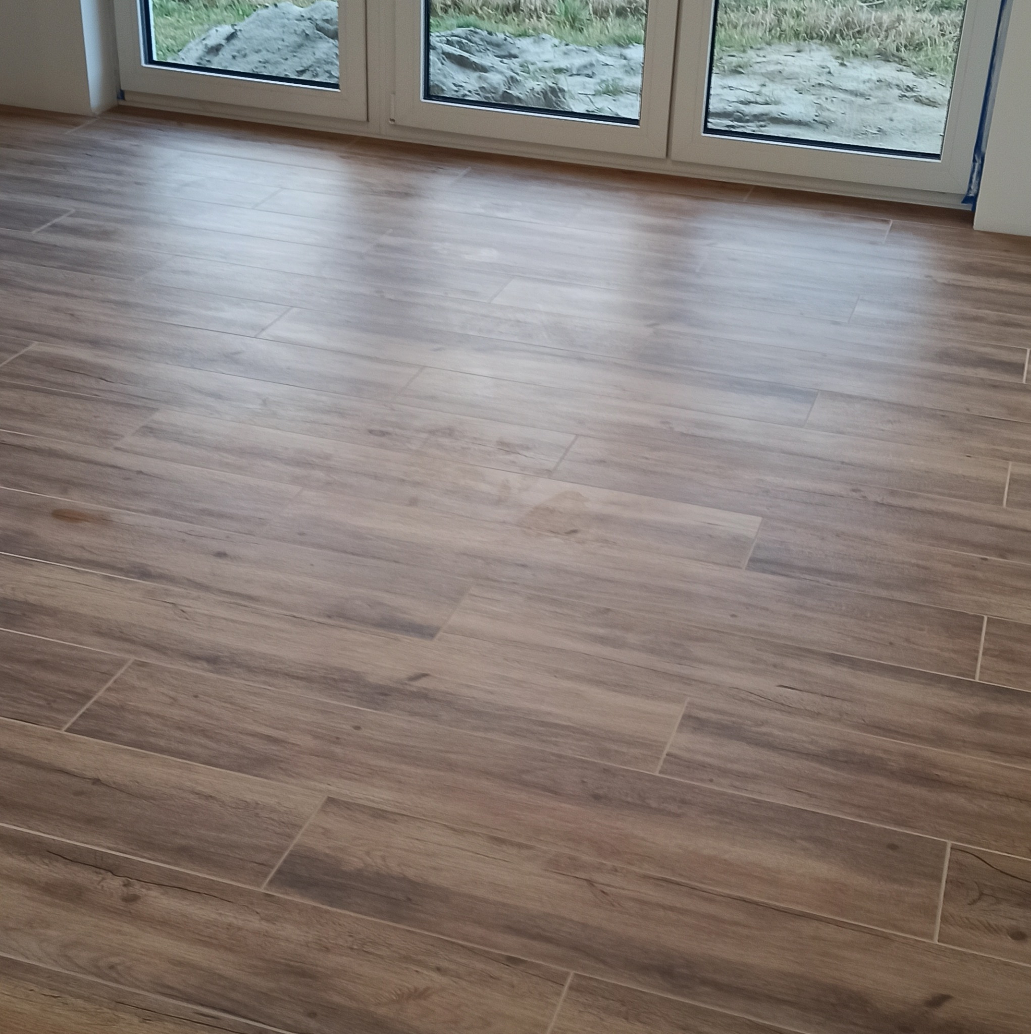 Ułożona pod kątem podłoga z płytek imitujących drewno, widok z góry na okno z widokiem na ziemię.